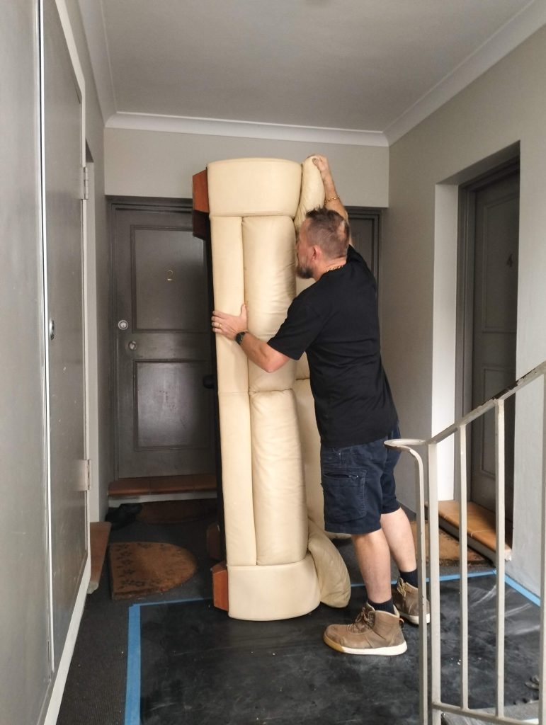 otg rubbish team member Mark in unit hallway holding leather lounge vertically up